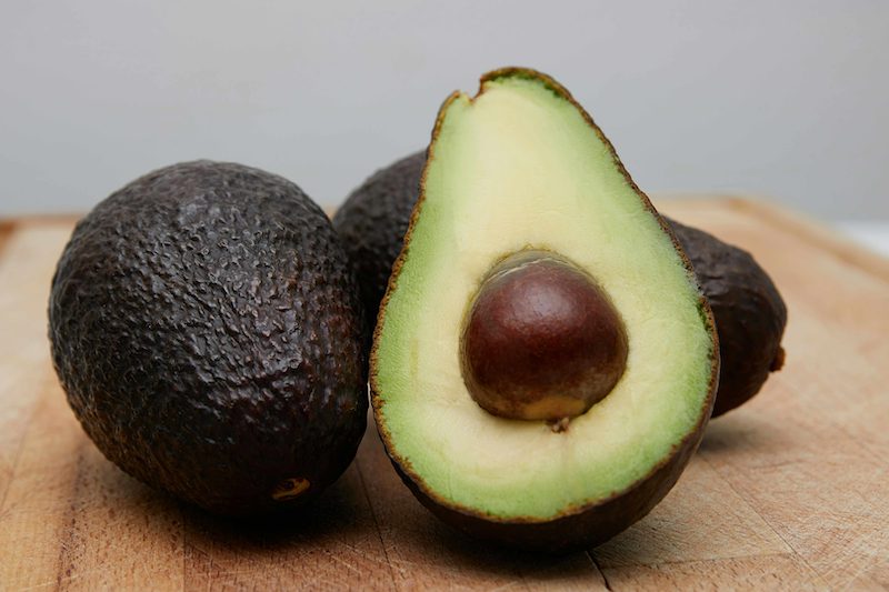 Three avocados on a wooden board, one cut in half to show the stone